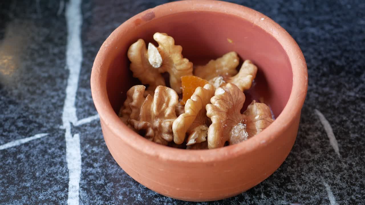 Hand placing candied fruit and walnuts into a terracotta bowl