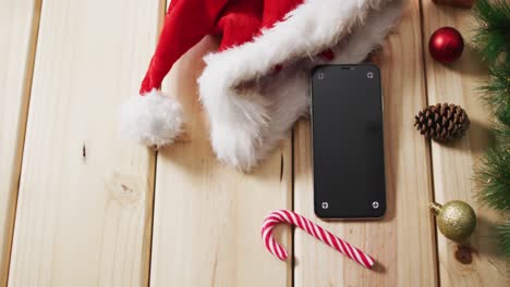 Vídeo-De-Adornos-Navideños-Con-Smartphone-Y-Gorro-De-Papá-Noel-Sobre-Fondo-De-Madera