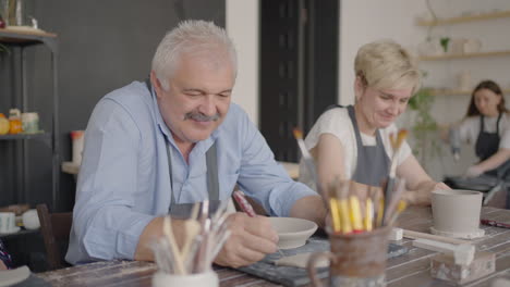 three elderly people work on a potter's wheel in slow motion