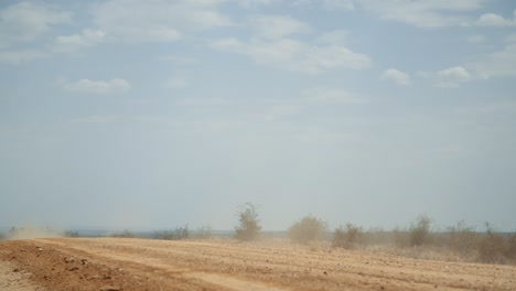 static wide shot of a off-roading vehicle driving past frame from right to left in africa as it leaves a dust trail