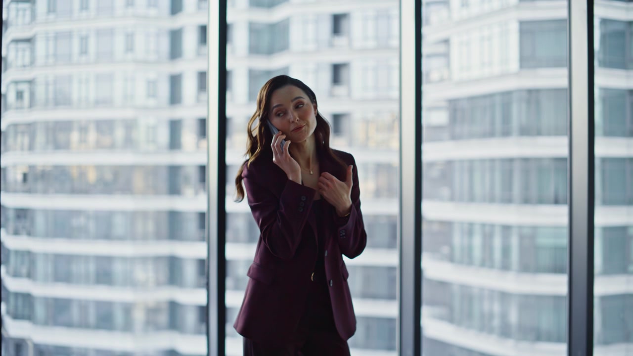Business manager speaking cellphone standing at panoramic window luxury office
