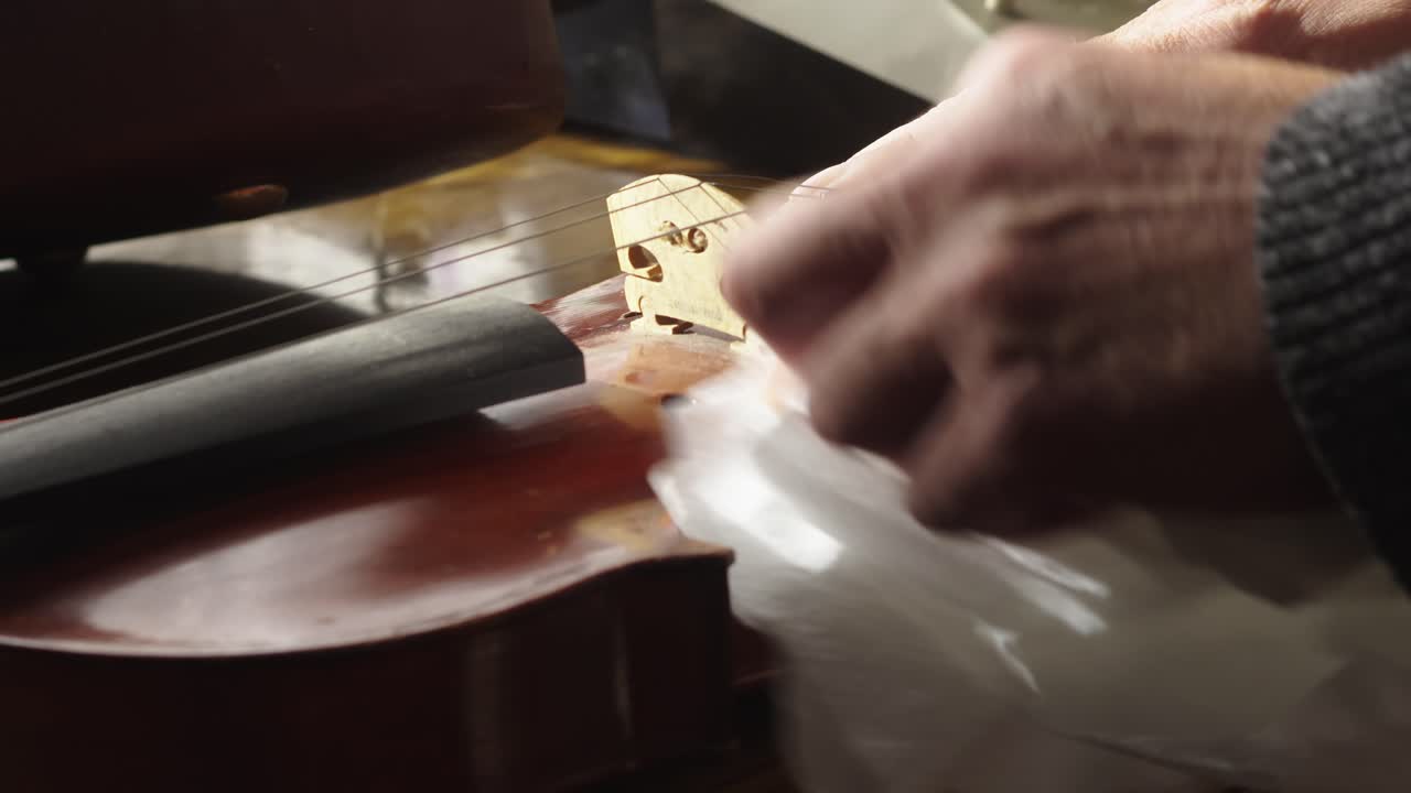 Primo piano di un musicista che pulisce l’antica cassa in legno di un violino