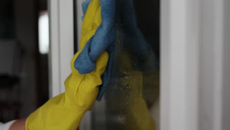 woman, housework and housekeeping concept - woman in gloves cleaning window with rag and cleanser spray at home