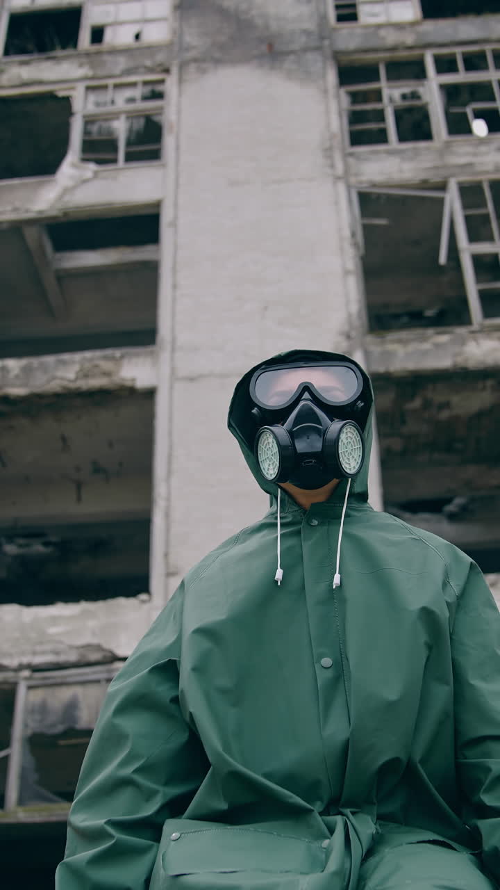 Portrait of a man in safety suit in radiation zone. Person in gas mask and protective uniform standing alone on ruined building background. Apocalypse concept. Vertical video