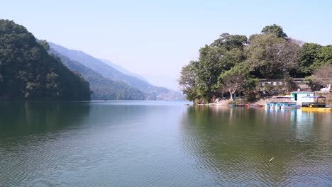 Slow-panning-shot-of-Fewa-lake-located-at-Pokhara,-Nepal-with-the-boats-parked-near-the-shore