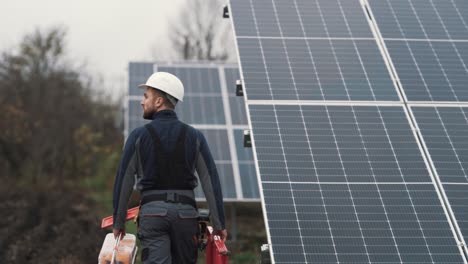 rear view of young man in work uniform with tools in hand inspecting solar panels