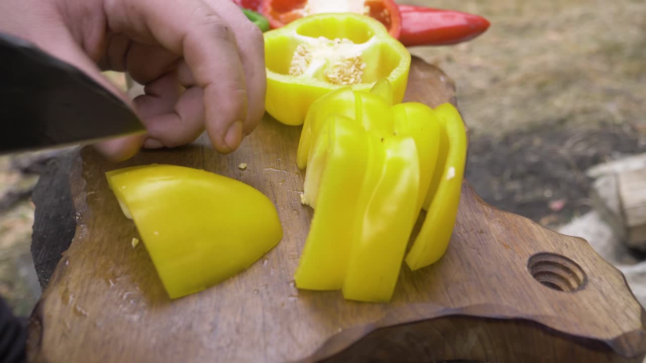 Chef cutting yellow bell peppers on a chopping board. Cut into small slices, slices of bell pepper. The shredder is oak-colored wood