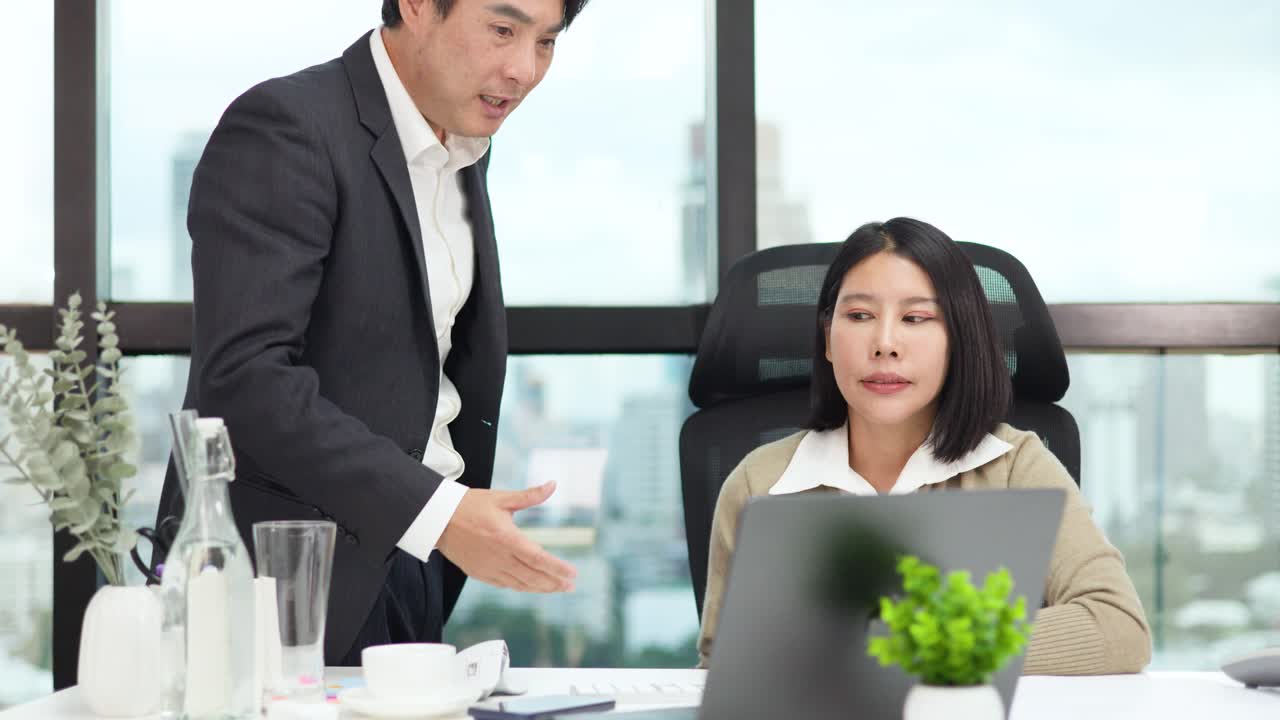 Male manager sternly critiques female employee at desk in modern office, natural daylight, mid-shot