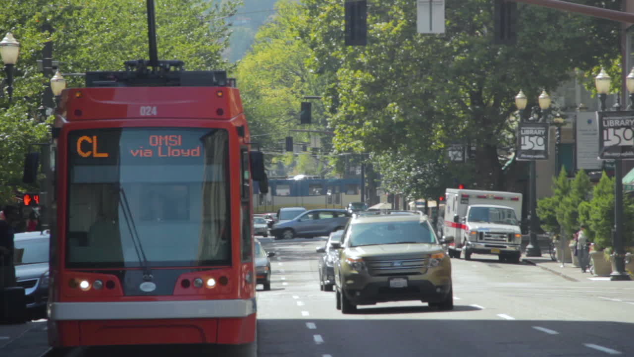 Telephoto view of a downtown Portland, Oregon, USA street with many cars and trains passing by on a sunny day.