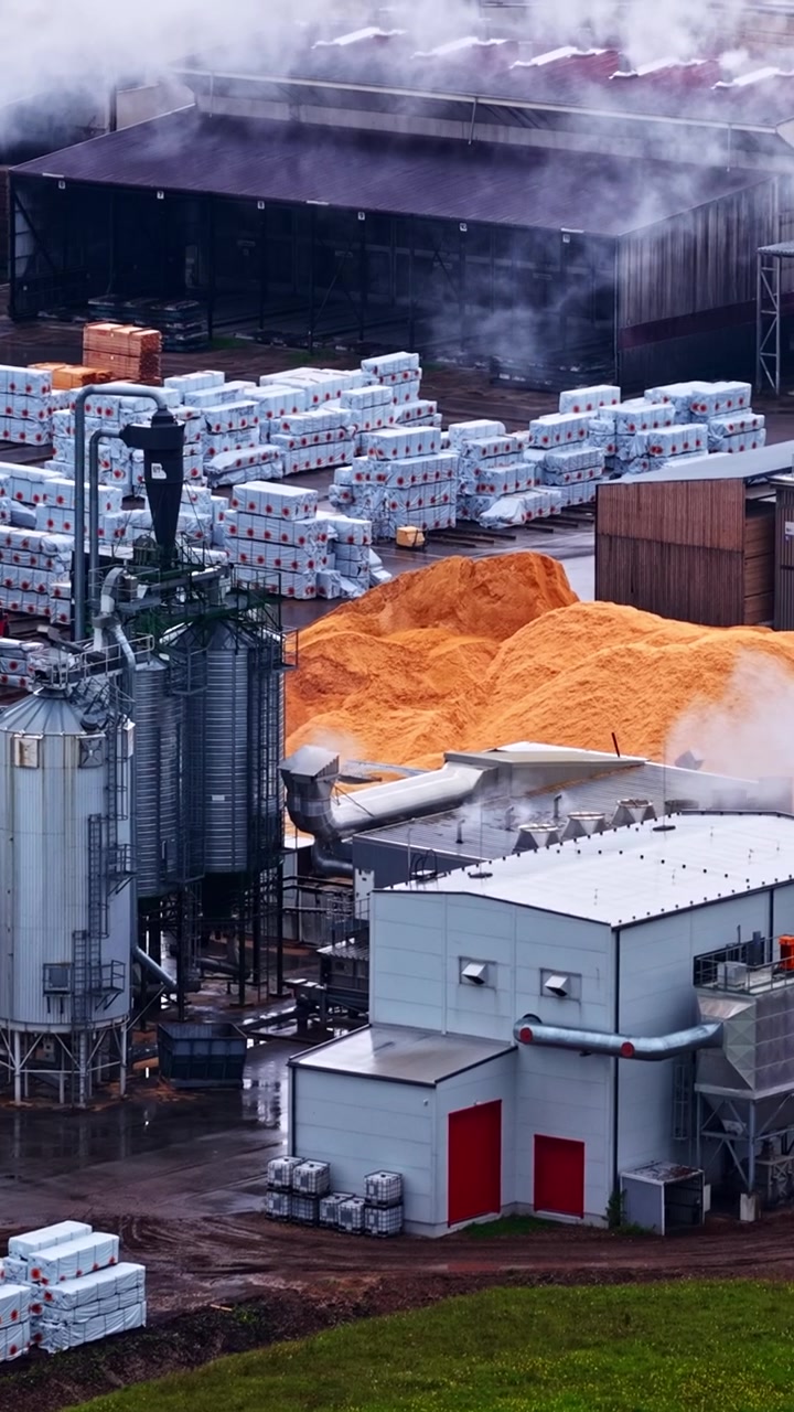 Industrielles Sägewerk mit Holzlagerung und Verarbeitungssilos in Lettland, vertikale Luftaufnahme.