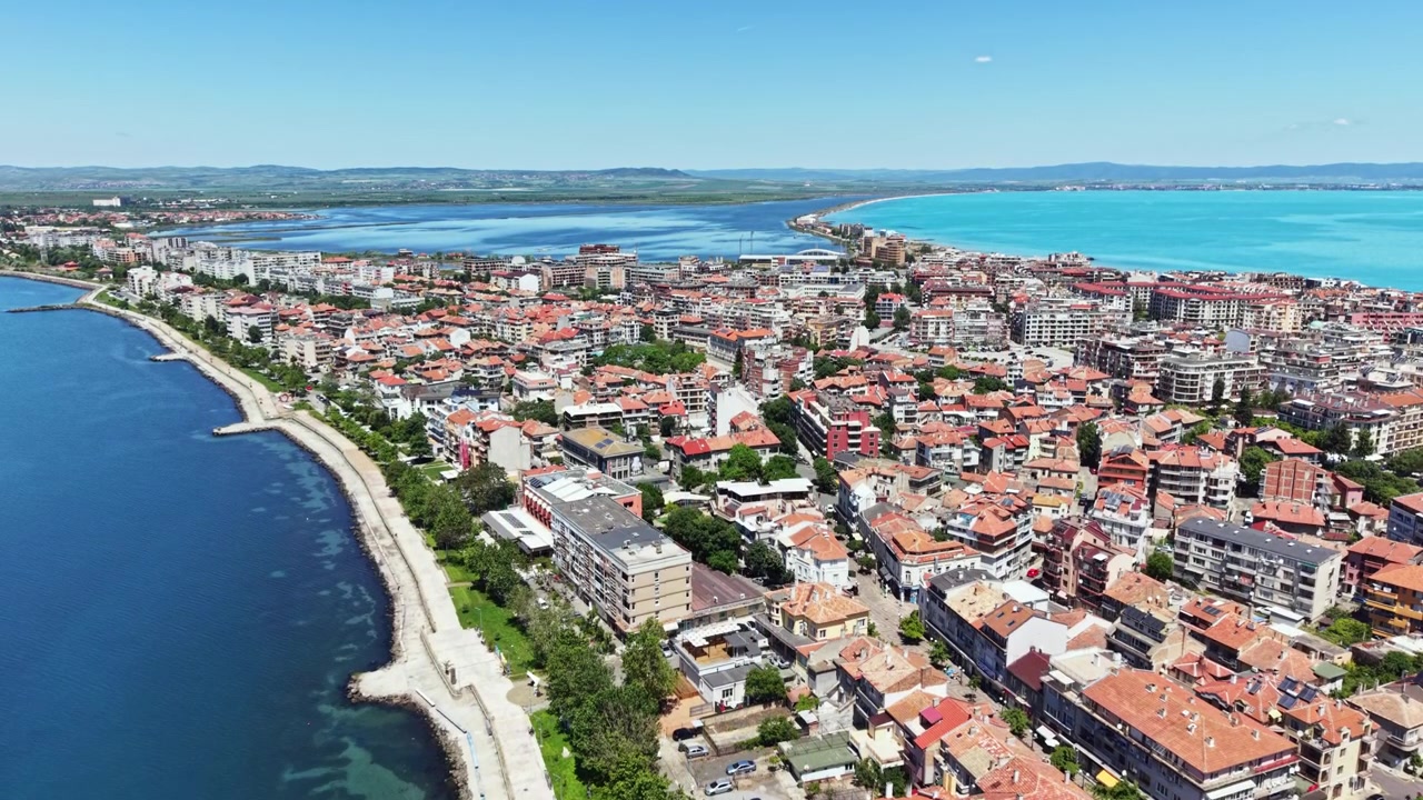 Vista della città con edifici lungo la costa e l'acqua durante una luminosa giornata estiva, mentre le persone si godono l'aria aperta ed esplorano la zona.