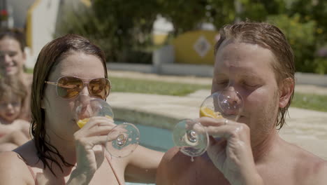 feliz esposa y esposo bebiendo cócteles y besándose en la piscina