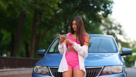 mujer usando un teléfono inteligente cerca de un coche azul