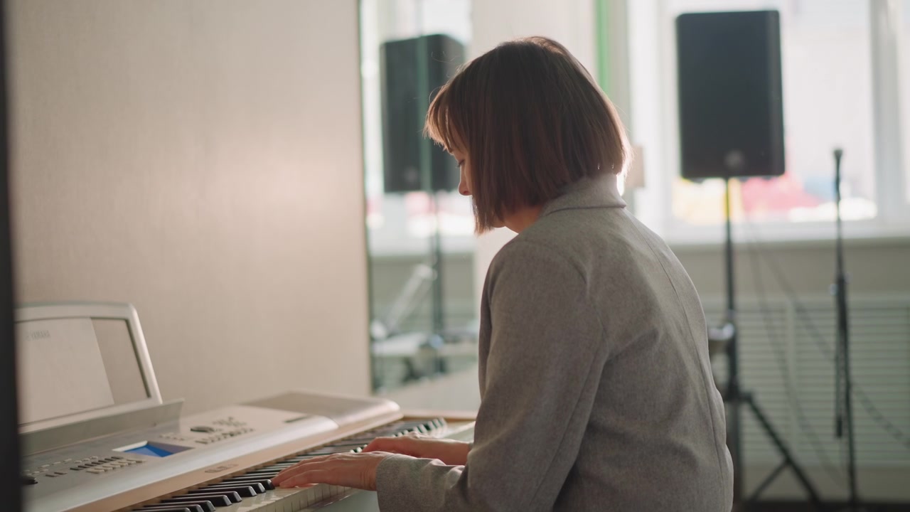 Sunlit classroom keyboard practice white female pianist coaching student through scales and warmup exercises, sunlight backlight, speaker in background, calm focused atmosphere, classroom setting