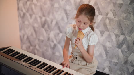 calm young girl in white top enjoys ice cream cone while practicing piano indoors, focused and composed, sitting in front of artistic gray patterned wall with soft lighting
