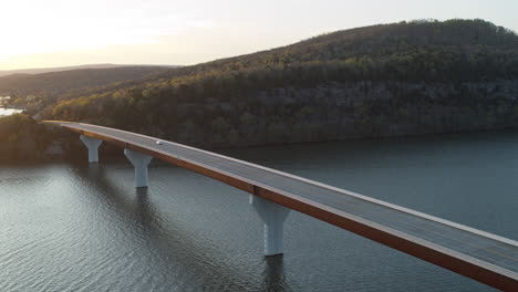 static aerial footage of a car driving across a bridge with a cliff and forest in the background during golden hour in tennessee