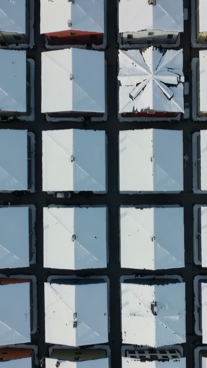 Vertical video: Surveying drone showing snow roofs on homes while moving south showing damaged roof