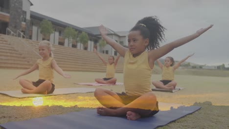 animation of sunset landscape over happy diverse schoolgirls stretching in outdoor yoga class