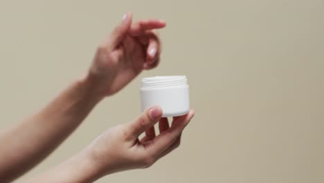 de manos de mujer sosteniendo crema en fondo beige con espacio de copia, cámara lenta