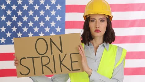 woman in hard hat holding an 'on strike' sign in front of an american flag