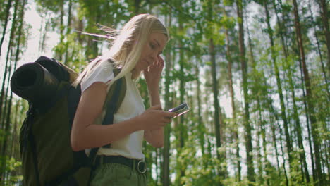 attractive woman relax in forest and using smartphone outdoors. woman hiking in the forest and typing message on smartphone. solo female hiker using smart phone.