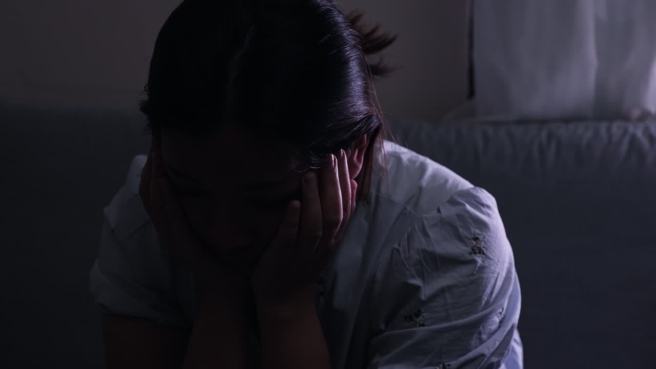 Mulher angustiada e deprimida com a mão no rosto e pescoço, chorando num quarto escuro