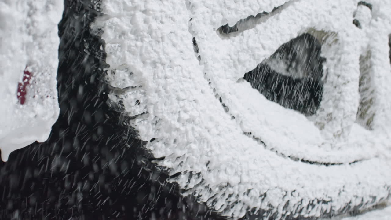 Close up of black car tire and silver rim being washed during cleaning process with soapy foam splashing across surface as water droplets drip down