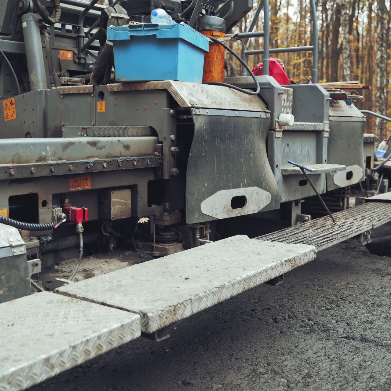 Heavy paver machine and workers put the hot asphalt on a street. Road construction workers with shovels in protective uniforms.