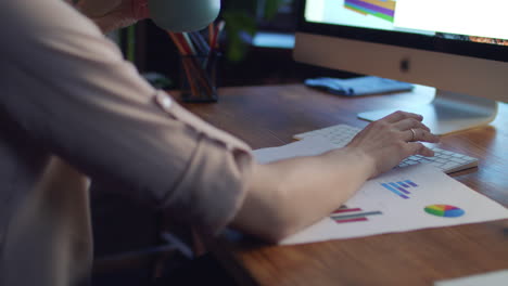 Weibliche-Hand-Hält-Kaffeetasse-Und-Arbeitet-Am-Computer-Am-Schreibtisch,-Rückansicht