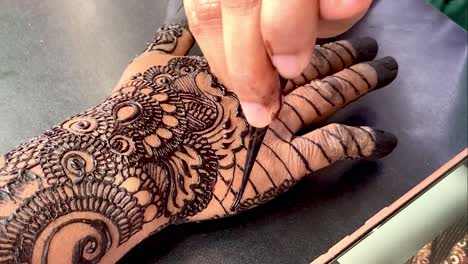 un acercamiento de una mano aplicando un hermoso diseño de arte de henna negra para una boda