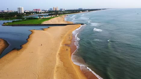 Drohnenaufnahmen-Eines-Strandes-Mit-Einem-Sich-öffnenden-Stauwasser-Und-Einer-Skyline-Der-Stadt-Mit-Hochhäusern-Im-Hintergrund