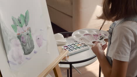 Vista-Trasera-De-Una-Chica-Rubia-Pintando-Una-Planta-Con-Un-Cepillo-En-Un-Atril-En-La-Sala-De-Estar-En-Casa-4