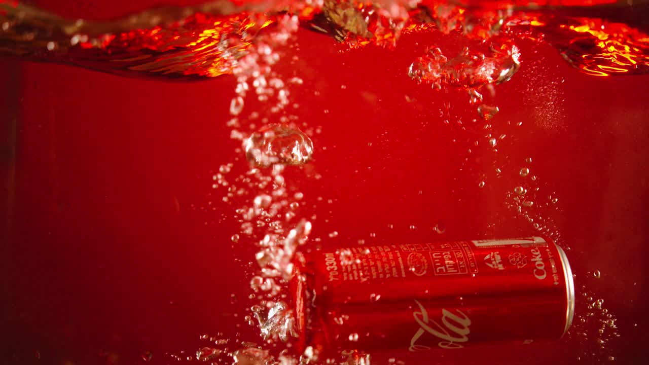 Cola can falls into a water tank in slow motion with a red background for use in advertisements