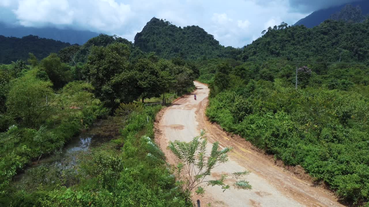 Immagine aerea statica di una motocicletta che avanza su una strada sterrata in una zona rurale nell'entroterra del Laos.