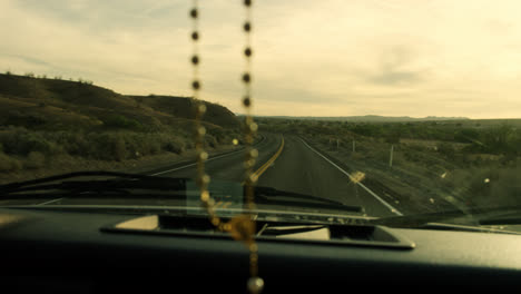 slow motion shot of road while driving in the middle of the desert, rosary hanging from the car mirror