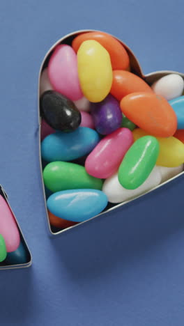 video of overhead view of multi coloured sweets in two heart shapes over blue background