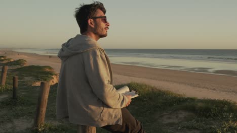 man reading book at seaside in summer