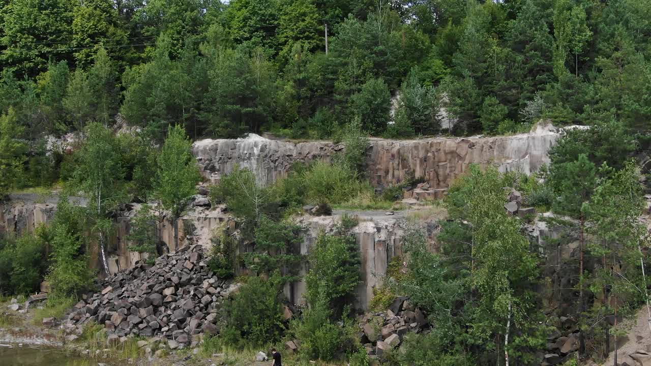 вид с воздуха на скальный карьер, окруженный деревьями, следящими слева