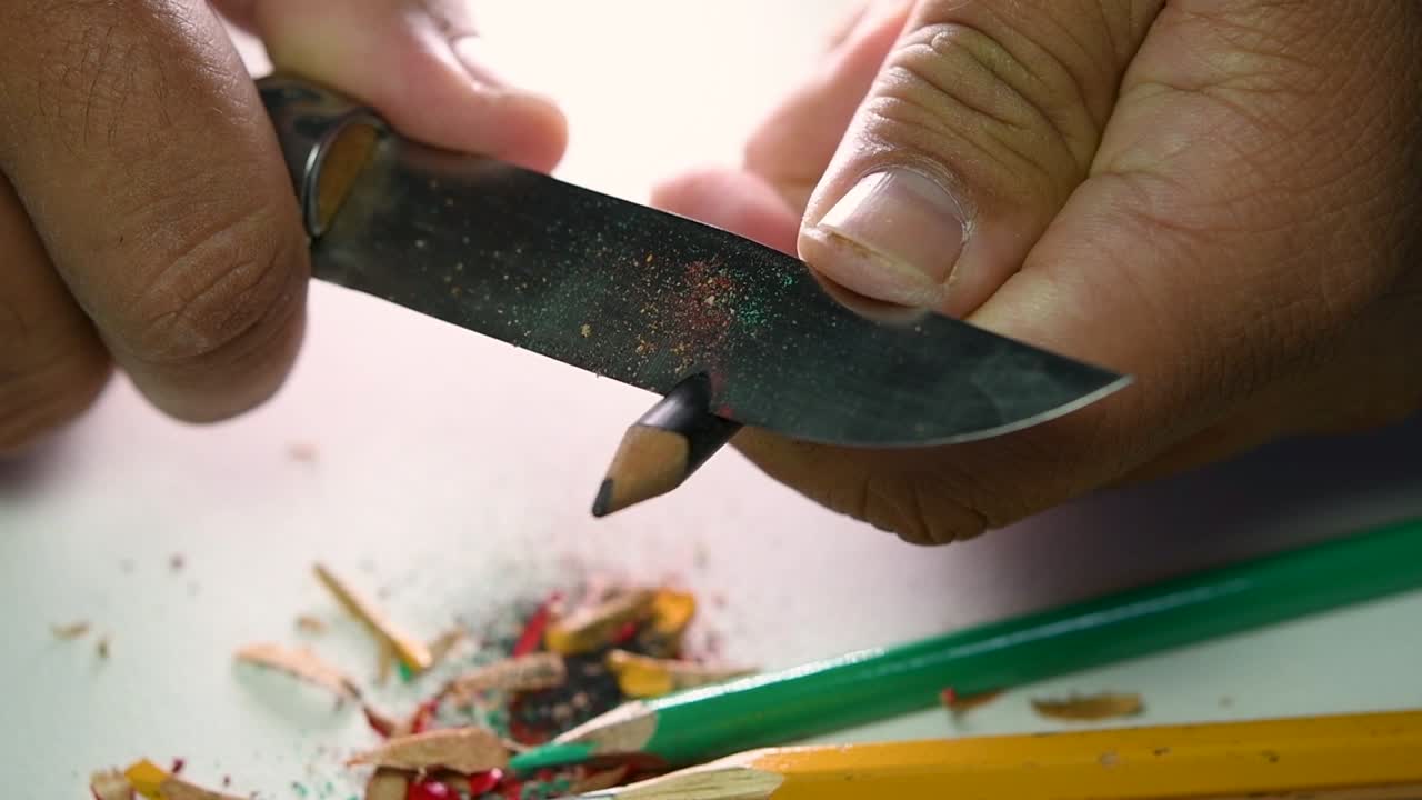 Opptak av hender som sakte spisser en blyant og noen fargeblyanter med en skarp kniv