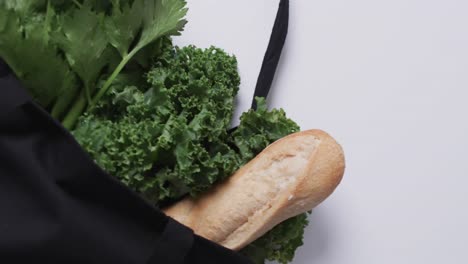 Video-of-black-canvas-bag-with-parsley,-kale-and-baguette,-copy-space-on-white-background