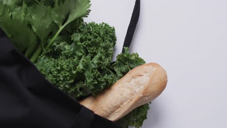 video of black canvas bag with parsley, kale and baguette, copy space on white background