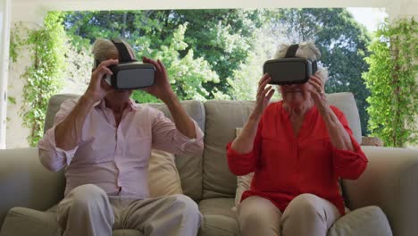 행복한 백인 노인 커플이 거실의 소파에 앉아 vr 헤드 ⁇ 을 벗고 웃고 있습니다.