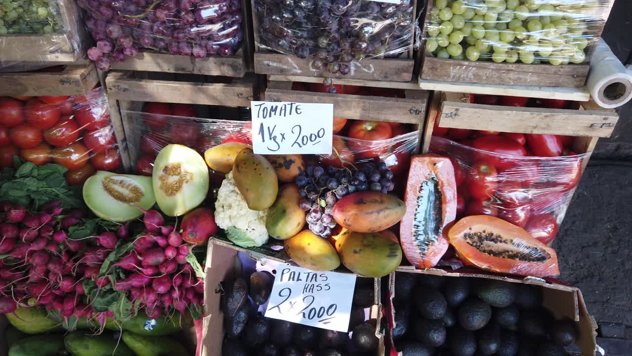 Primo piano di frutta e verdura in un mercato sudamericano, esposti con i prezzi in Argentina: melone verde, pomodori, mango, avocado e uva.