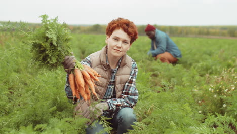 portrait of young female farmer with bunch of freshly harvested carrots