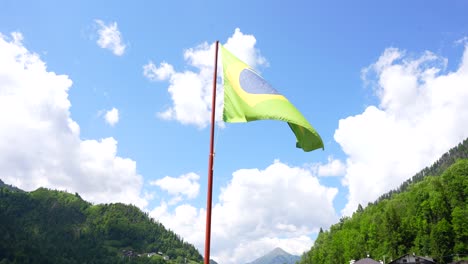 brazilian flag starts waving by the wind in a sunny day with clouds in alleghe, italy