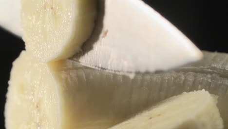 cutting a banana on a black stool and a black background with a chef's knife, high quality sexy close-up, food porn 4k