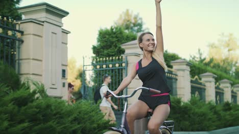 cheerful woman bicyclist enjoying cycling and rising up hand in summer park