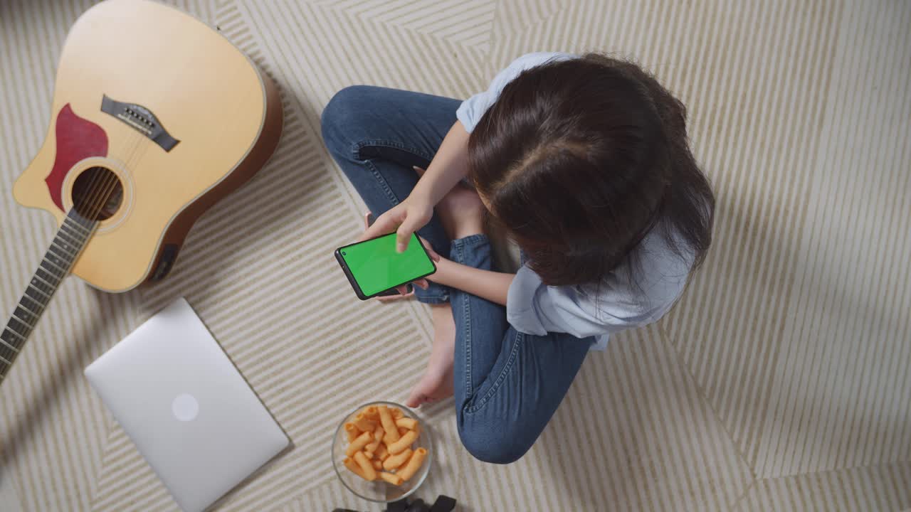 집 바닥에 카에 앉아서 녹색 화면 스마트폰을 사용하는 아시아 십대 소녀의  뷰