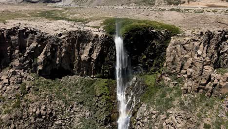 vista aérea de una toma de grúa de la cascada invertida con un arco iris que aparece a lo largo de su camino en un día soleado en maule, chile