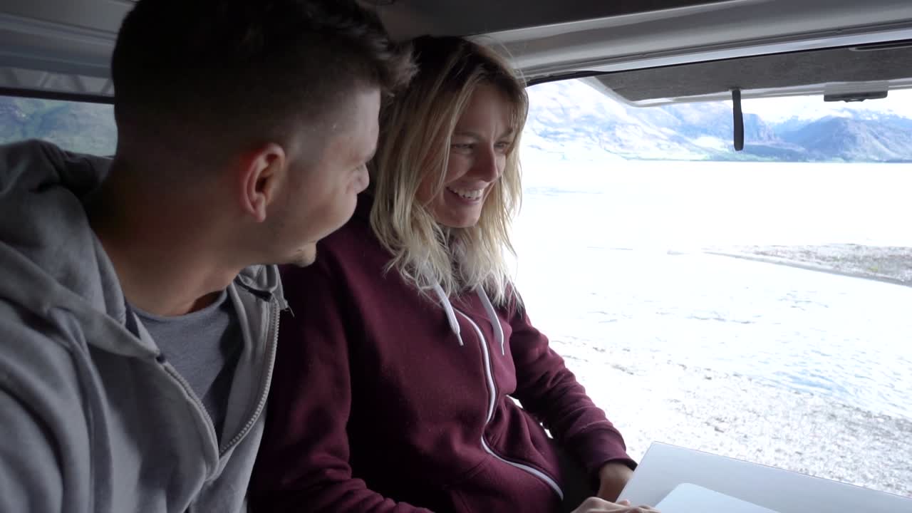 SLOWMO - Young atrractive couple digital nomads working in back of motorhome by Lake Wakatipu, Queenstown, New Zealand